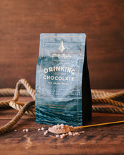 Load image into Gallery viewer, Belize Drinking Chocolate Bag with a small spoon of drinking chocolate mix in the forefront on a wooden background with a rope in the background.