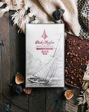 Load image into Gallery viewer, Black Fig packaging in front of an unpackaged Black Fig chocolate bar on a wooden background with dried figs and white cloth as decoration