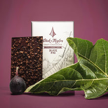 Load image into Gallery viewer, Unpackaged Black Fig bar in front of Black Fig packaging with a whole fig fruit and fig leaf as deocoration on a purple background.