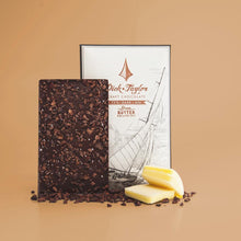 Load image into Gallery viewer, Unpackaged Brown Butter bar in front of Brown Butter bar packaging with butter slices and cacao nibs in the forefront on an orange background.