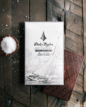 Load image into Gallery viewer, Fleur de Sel bar packaging on top of an unpackaged Fluer de Se bar next to a small bowl of salt on a wooden background.
