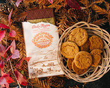 Load image into Gallery viewer, An opened Ginger Snap bar next to a basket of ginger snap cookies on a background of leaves, tree needles, and pine cones.
